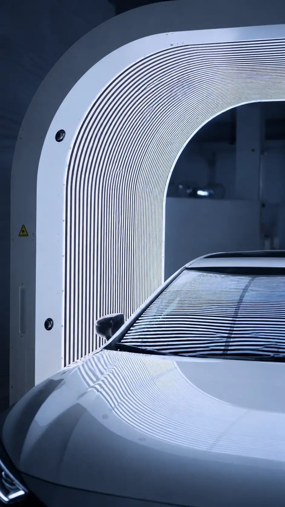 A white car beneath an arch scanner with striped light reflected across its hood and windshield