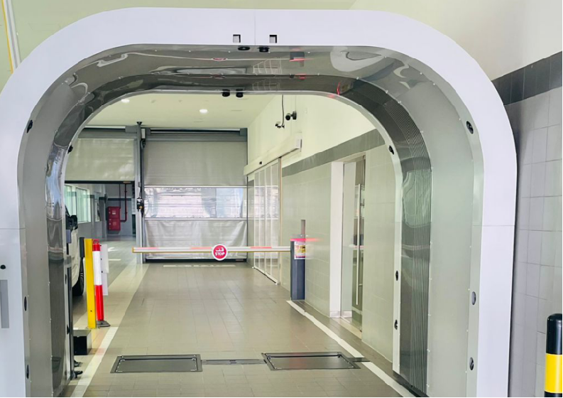 A mirrored arch scanner with floor plates in an indoor inspection lane leading to a barrier gate