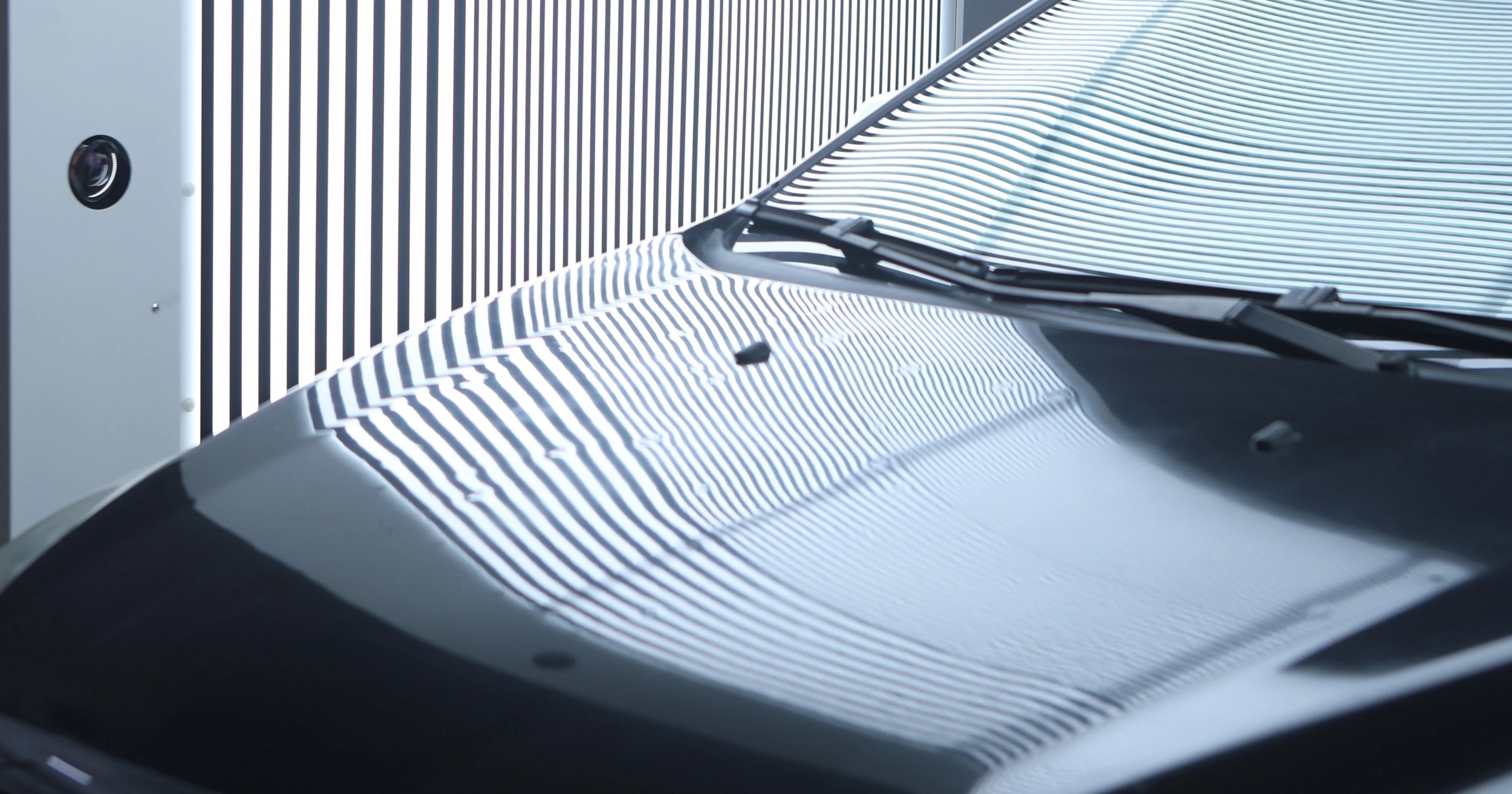 Close view of striped light from an arch scanner reflecting across a dark car's hood