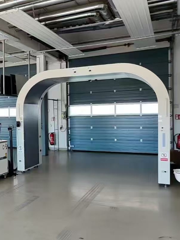 White drive-through arch scanner standing in a test hall in front of blue roller doors