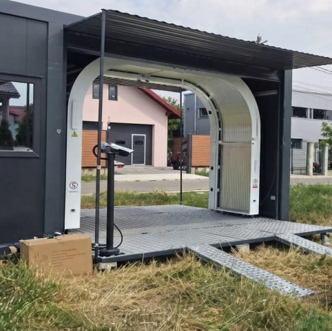 Mobile hail damage scanner arch under a container canopy with metal ramps on grass