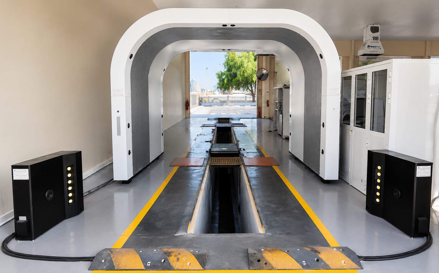 Empty indoor drive-through inspection lane with a white arch scanner standing over an inspection pit and black scanning units on both sides of the lane
