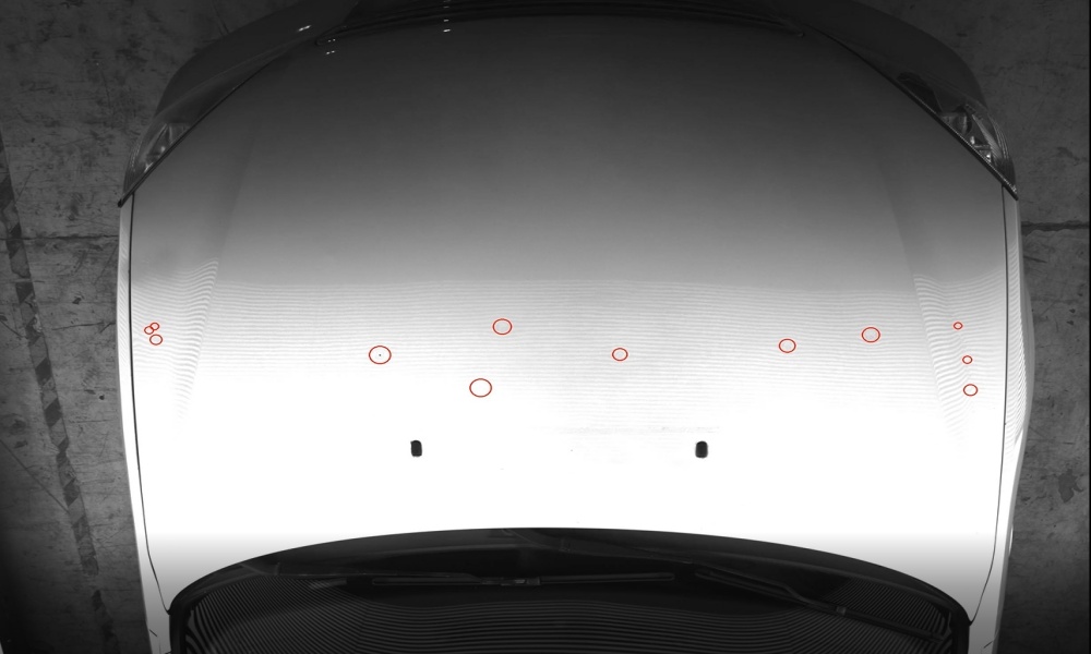 Top-down grayscale view of a car hood with red circles marking detected dents